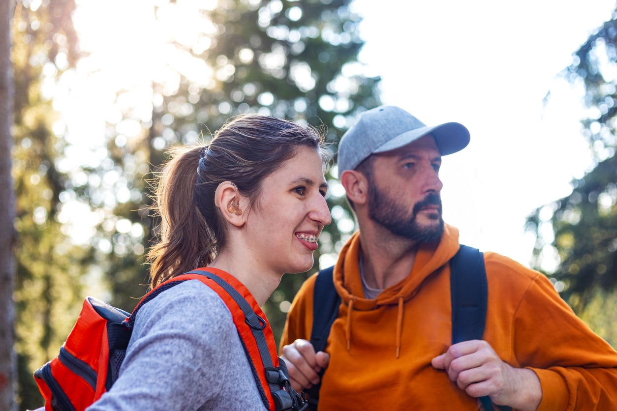 Young girl wearing hearing aids on a hike with her dad.