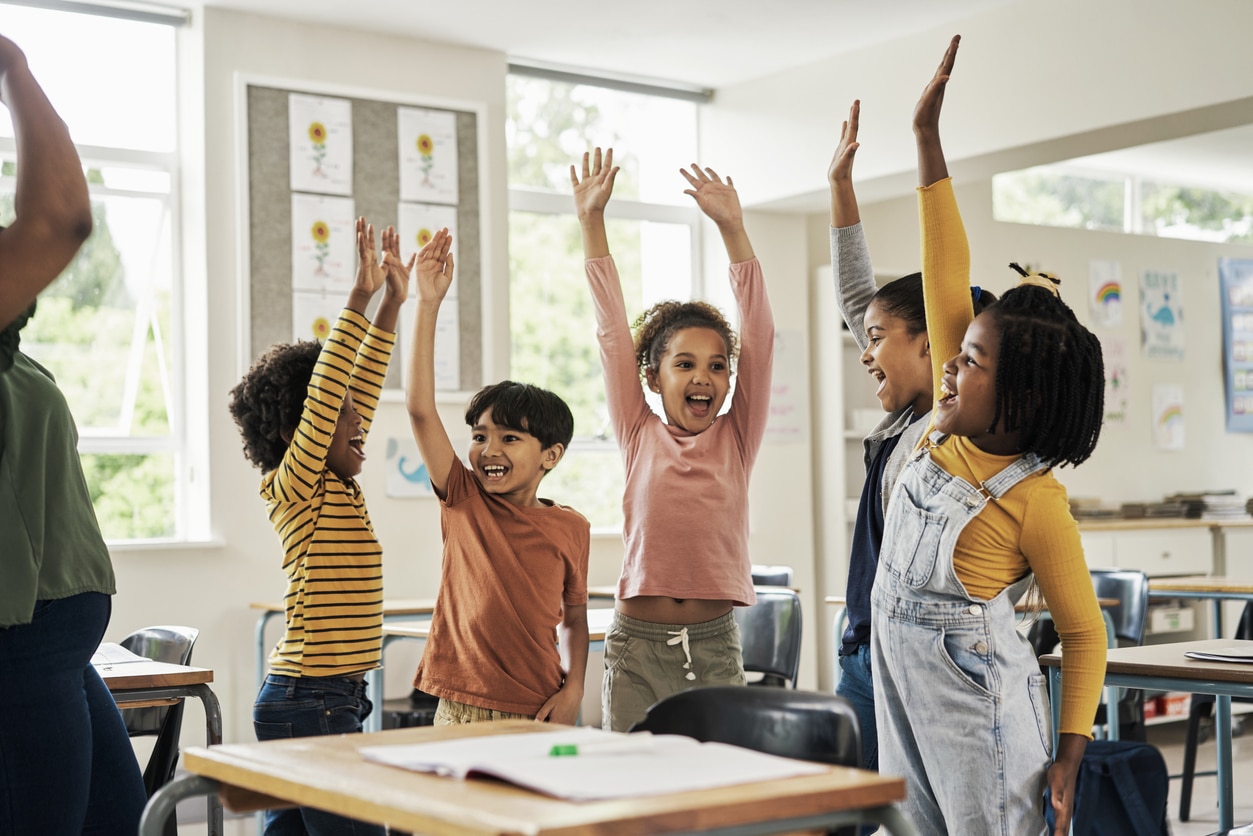 Happy kids holding their hands up in class