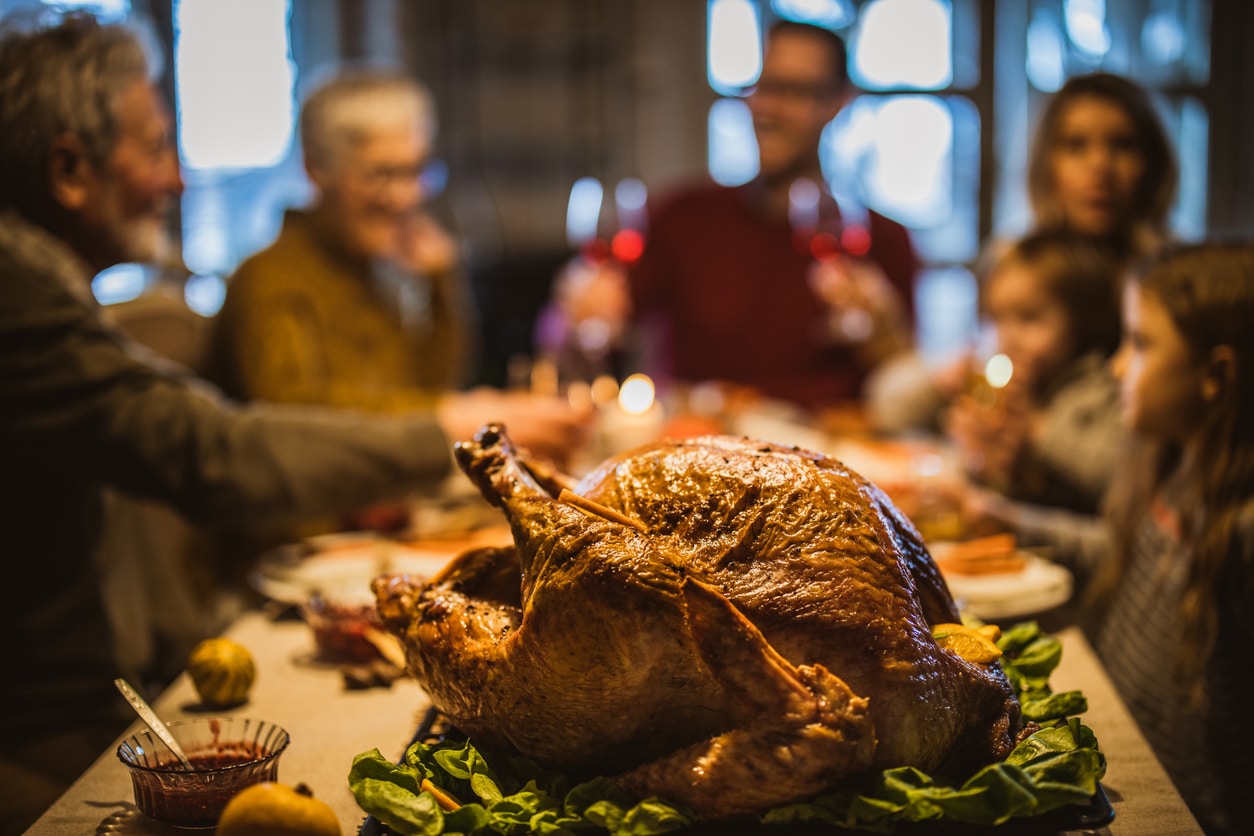 Family sits down for thanksgiving dinner, focused shot on the turkey