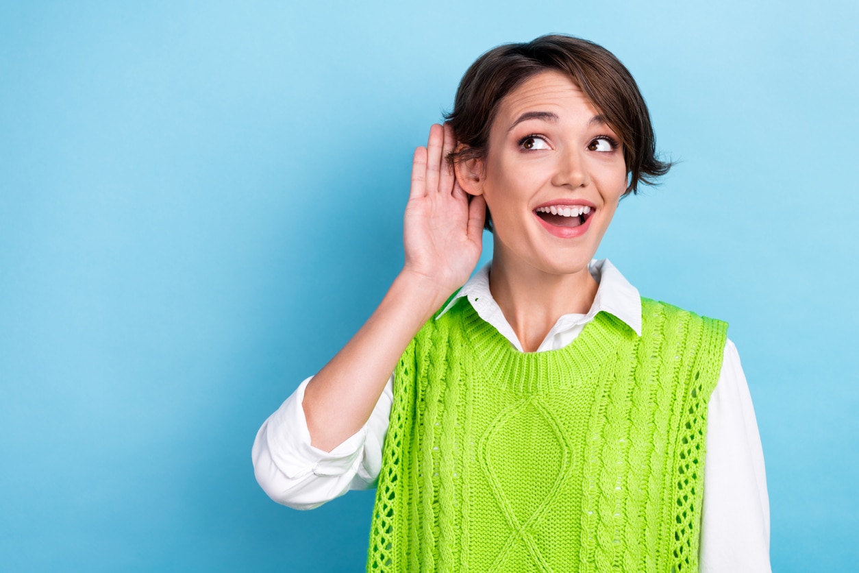 Happy woman with her hand to her ear on a blue background