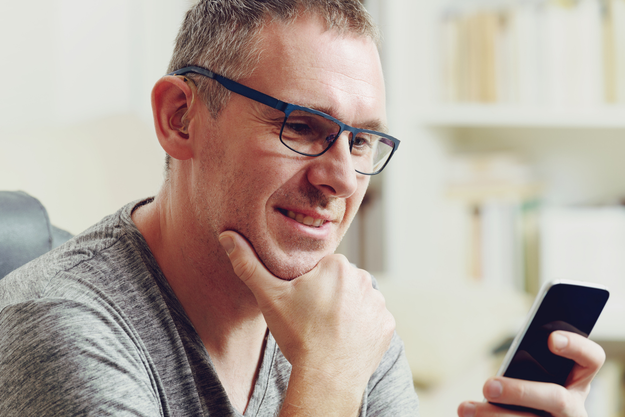 Man with hearing aids looks at phone